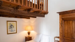 Une chambre à coucher avec un lit, une table de chevet avec une lampe, une chaise en bois, une armoire et un tableau accroché au mur.