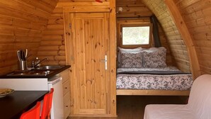 Ett kompakt, träinrett utrymme med ett köksområde, ett matbord med stolar, en säng och ett fönster som släpper in naturligt ljus.