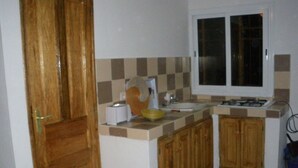 A kitchen with a wooden door, a window, a sink, and cabinets. - Villa pirogue: The huts of Saly (M bour)