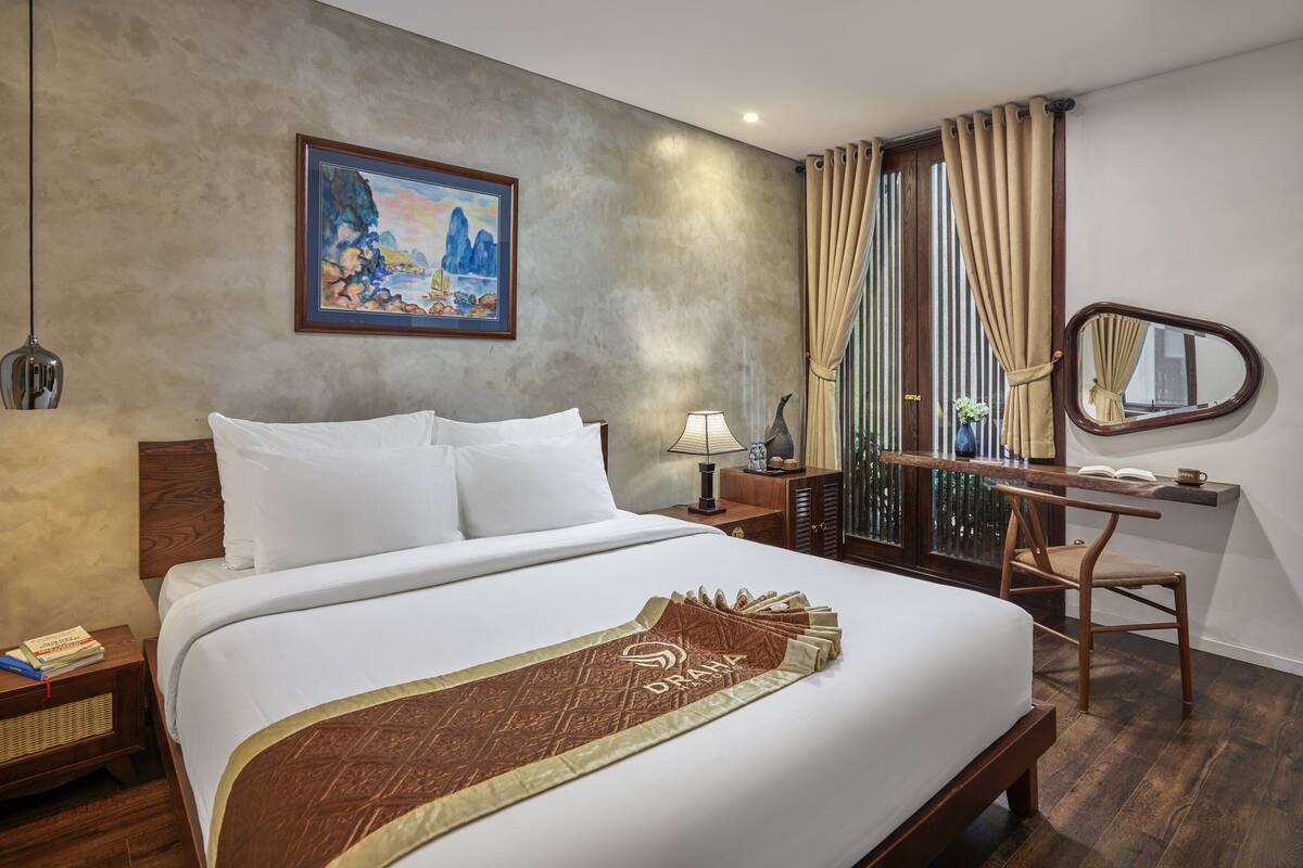 A hotel room with a large bed, a desk, a chair, a lamp, a mirror, and a painting on the wall.