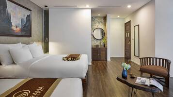 Quarto de hotel com uma cama grande, uma mesinha com um vaso e uma revista, uma cadeira e um quadro na parede.