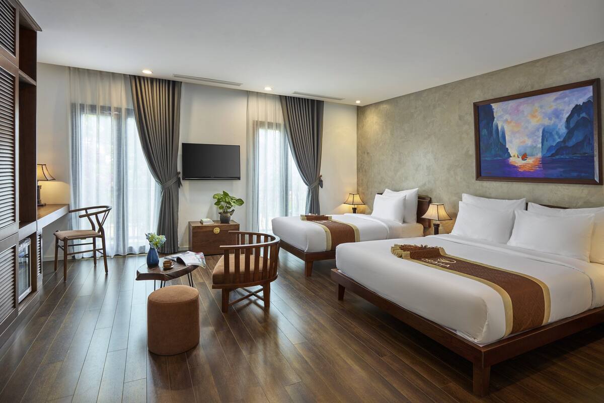 A hotel room with two beds, a desk, a chair, a TV, and a painting on the wall.