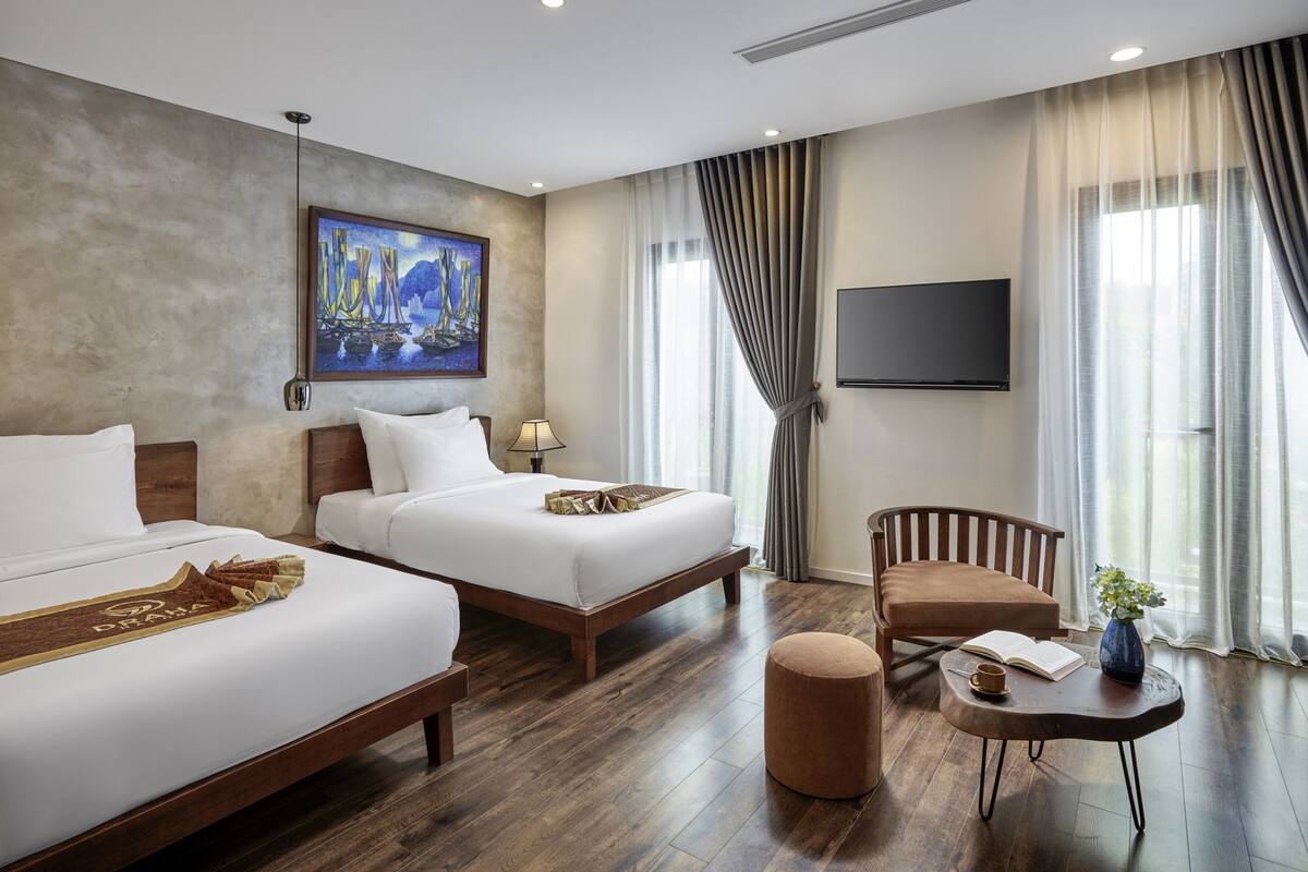 A hotel room with two beds, a TV, a desk with a chair, and a painting on the wall.