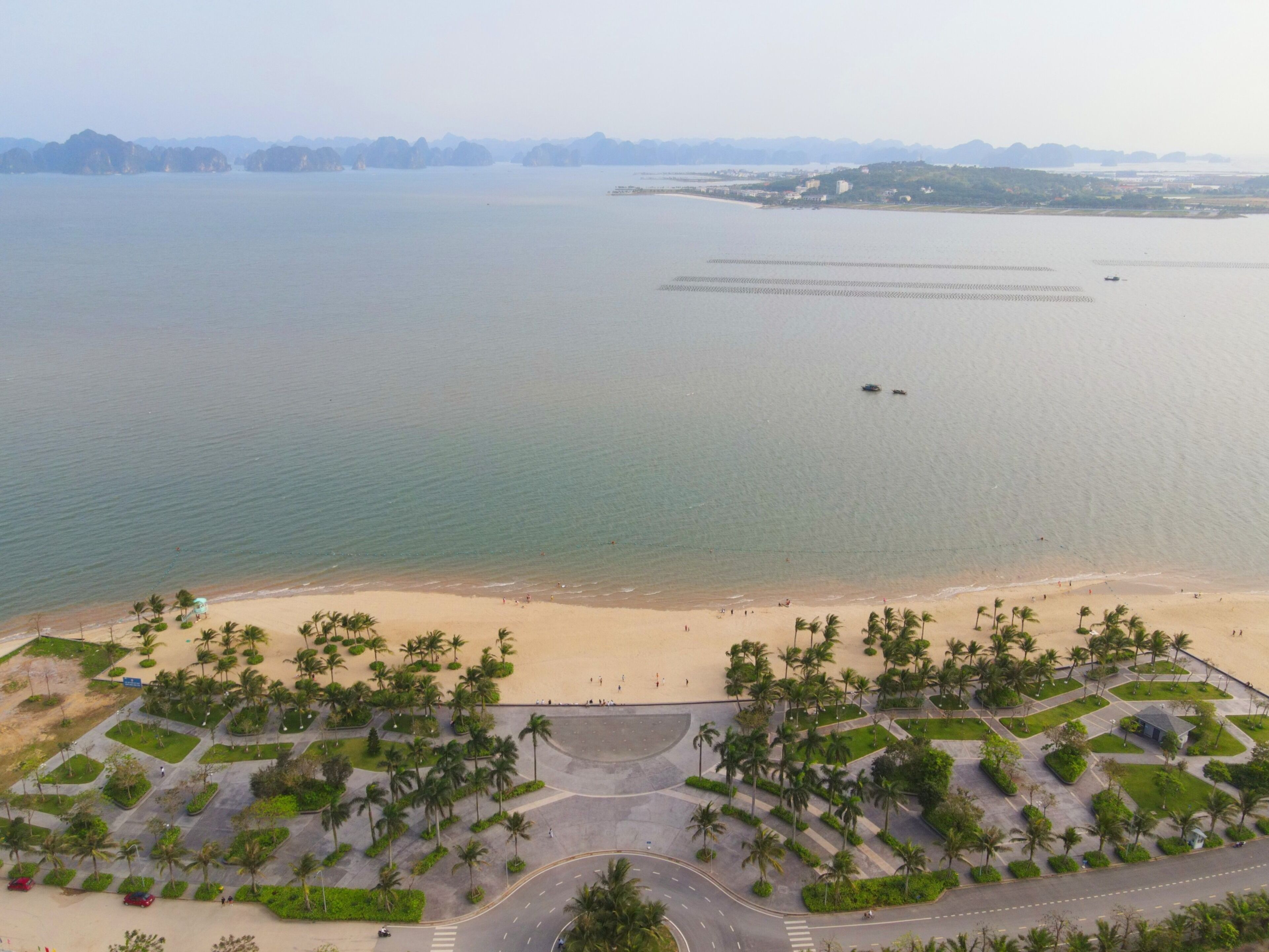 An aerial view of a coastal area with a beach, palm trees, and a road leading to the beach.