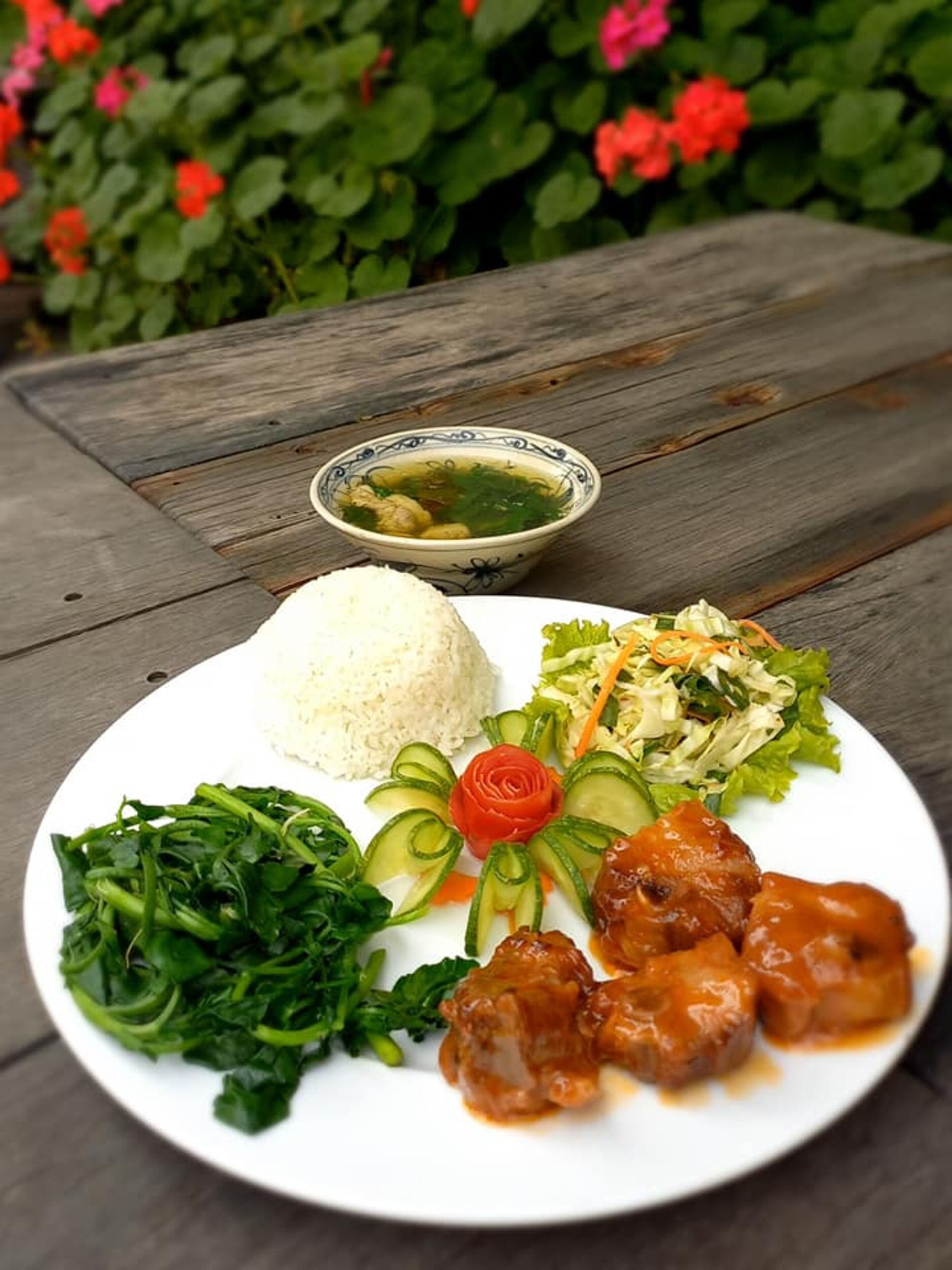 Un plato de comida con arroz, verduras y carne, sobre una mesa de madera al aire libre.