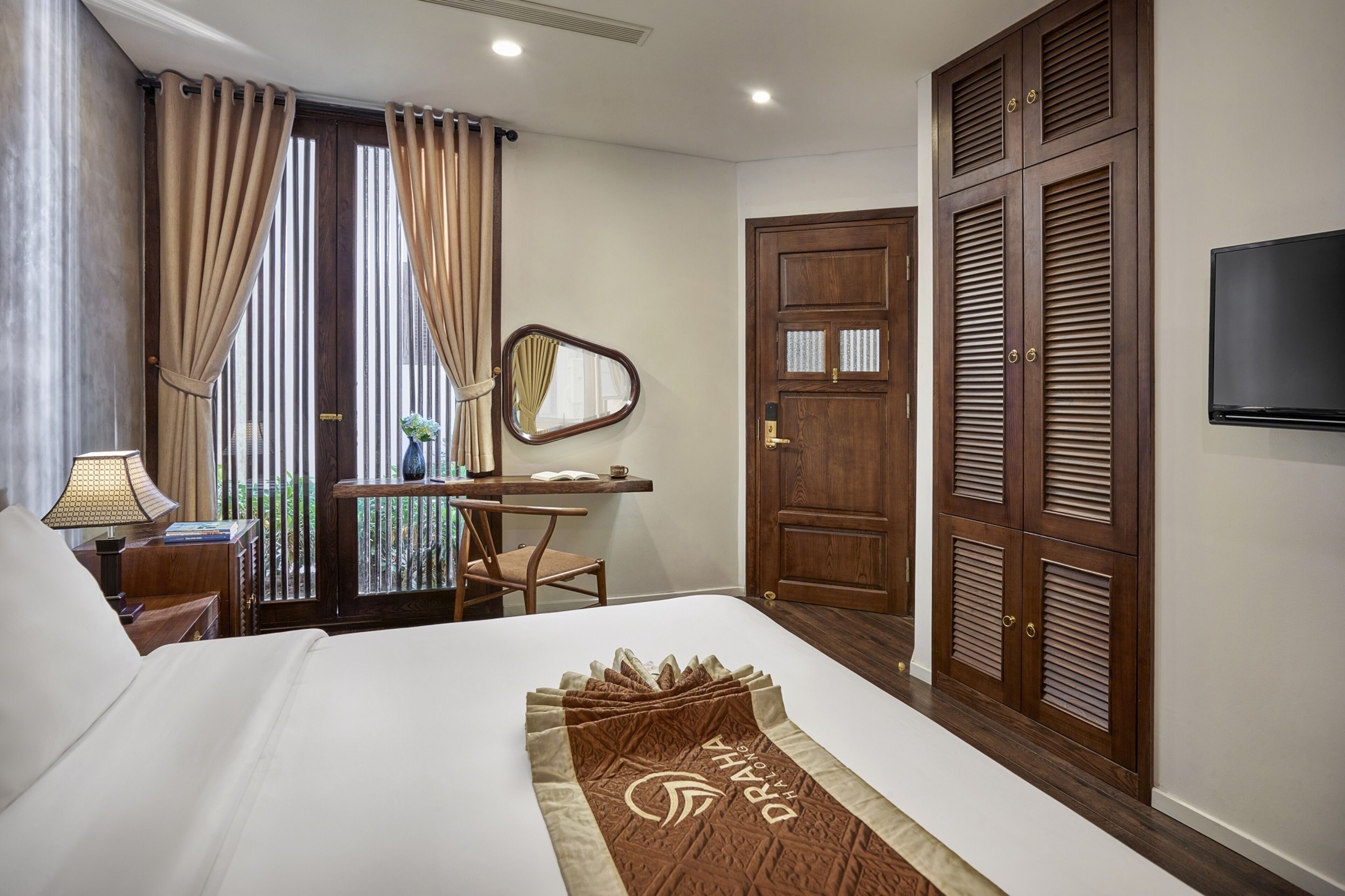 A hotel room with a bed, a desk with a chair, a mirror, a wardrobe, and a TV.