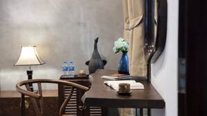 Une chambre d’hôtel avec un bureau en bois, une lampe, un vase avec des fleurs, une bouteille d’eau et un livre.
