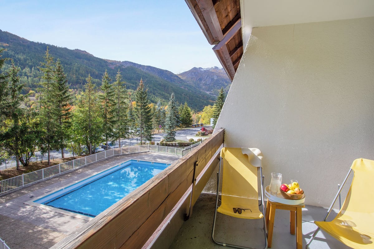 A balcony with a pool, a chair, and a table with fruit and a pitcher.