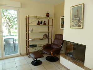 A living room with a brown leather chair, a glass-top coffee table, a fireplace, and a bookshelf with decorative items.