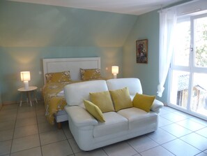 A bedroom with a bed, a white sofa, two bedside lamps, and a window with curtains.