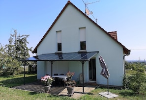 A single-story house with a sloped roof, a covered patio with a table and chairs, and a potted plant.