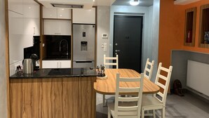 A modern kitchen with a built-in island, a black refrigerator, and a wooden dining table with white chairs. - Apartment, Le Saint Simon rated 3 stars (Aix-les-Bains)