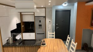 A compact kitchen with modern appliances, a dining area with a wooden table and white chairs, and a black door. - Apartment, Le Saint Simon rated 3 stars (Aix-les-Bains)