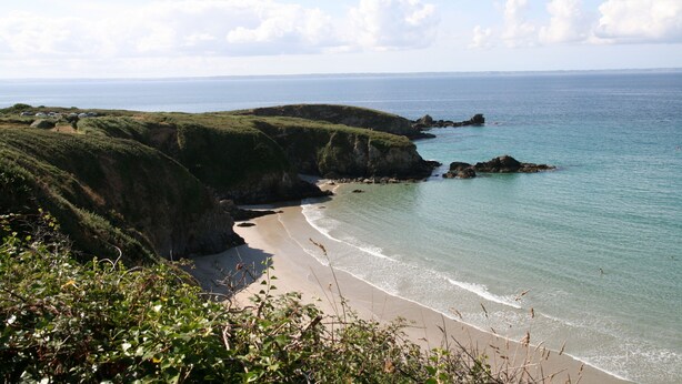 A coastal landscape with a sandy beach, grassy cliffs, and calm sea.