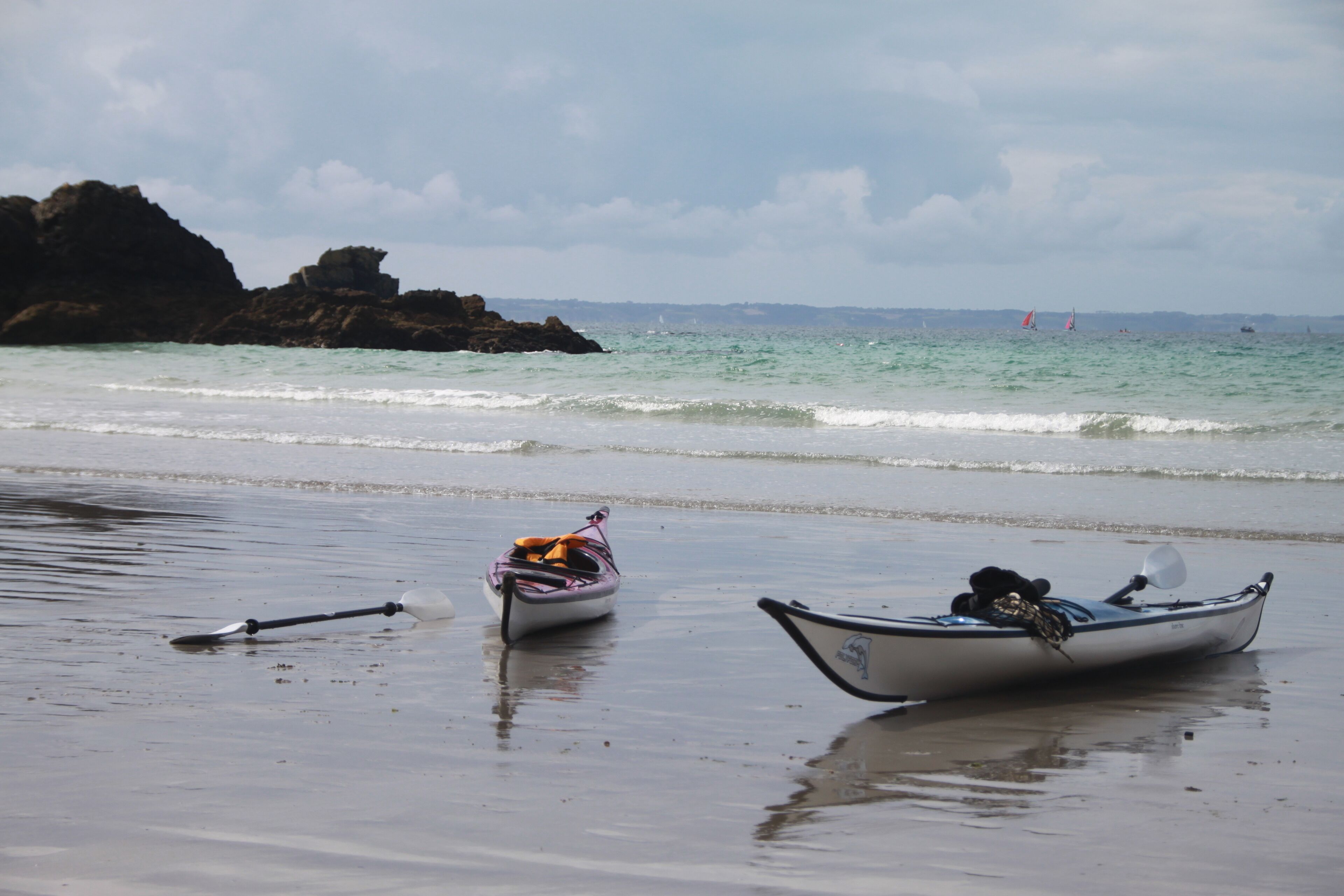 Two boats on a sandy beach with a rocky outcrop in the background and a calm sea.