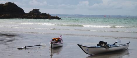 Two boats on a sandy beach with a rocky outcrop in the background and a calm sea.