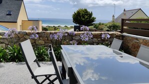 An outdoor patio with a glass table and chairs, a stone wall, and a view of the ocean.