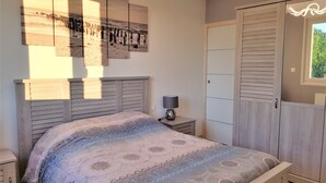 A bedroom with a bed, bedside table, lamp, wardrobe, and artwork on the wall.