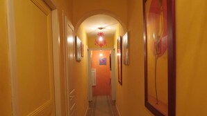 Um corredor com piso de madeira, paredes amarelas e luminária no teto.
