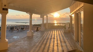 Un espacio al aire libre cubierto con vista a la puesta de sol sobre el mar, que incluye columnas y una barandilla.