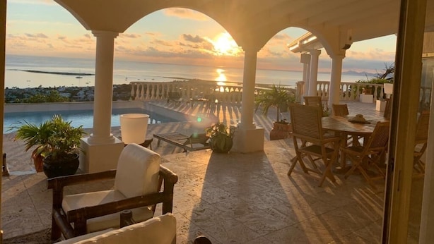 Un espacio de estar al aire libre con techo y vistas al atardecer sobre el mar.