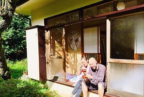 Um casal sentado em um banco de madeira em frente a um prédio com janelas amplas e um relógio.