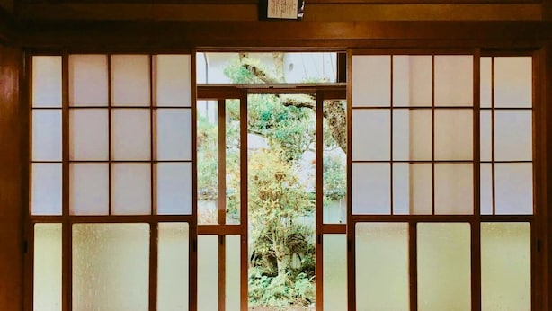 Een traditionele Japanse kamer met tatami vloerbedekking, een laag houten bed en uitzicht op een tuin door middel van shoji schermen.
