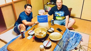 Twee personen zitten aan een tafel met een bord waarop 'Vanguard Backpackers Y' staat.