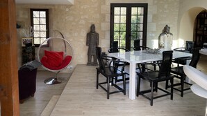 A dining area with a white table and black chairs, a hanging chair with red cushions, and two statues. - Pretty character house with swimming pool in Entre deux Mers (min. 5 nights) (Romagne)