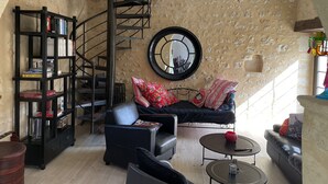 A cozy living room with a black leather sofa, a black metal bookshelf, a round mirror, and a spiral staircase. - Pretty character house with swimming pool in Entre deux Mers (min. 5 nights) (Romagne)