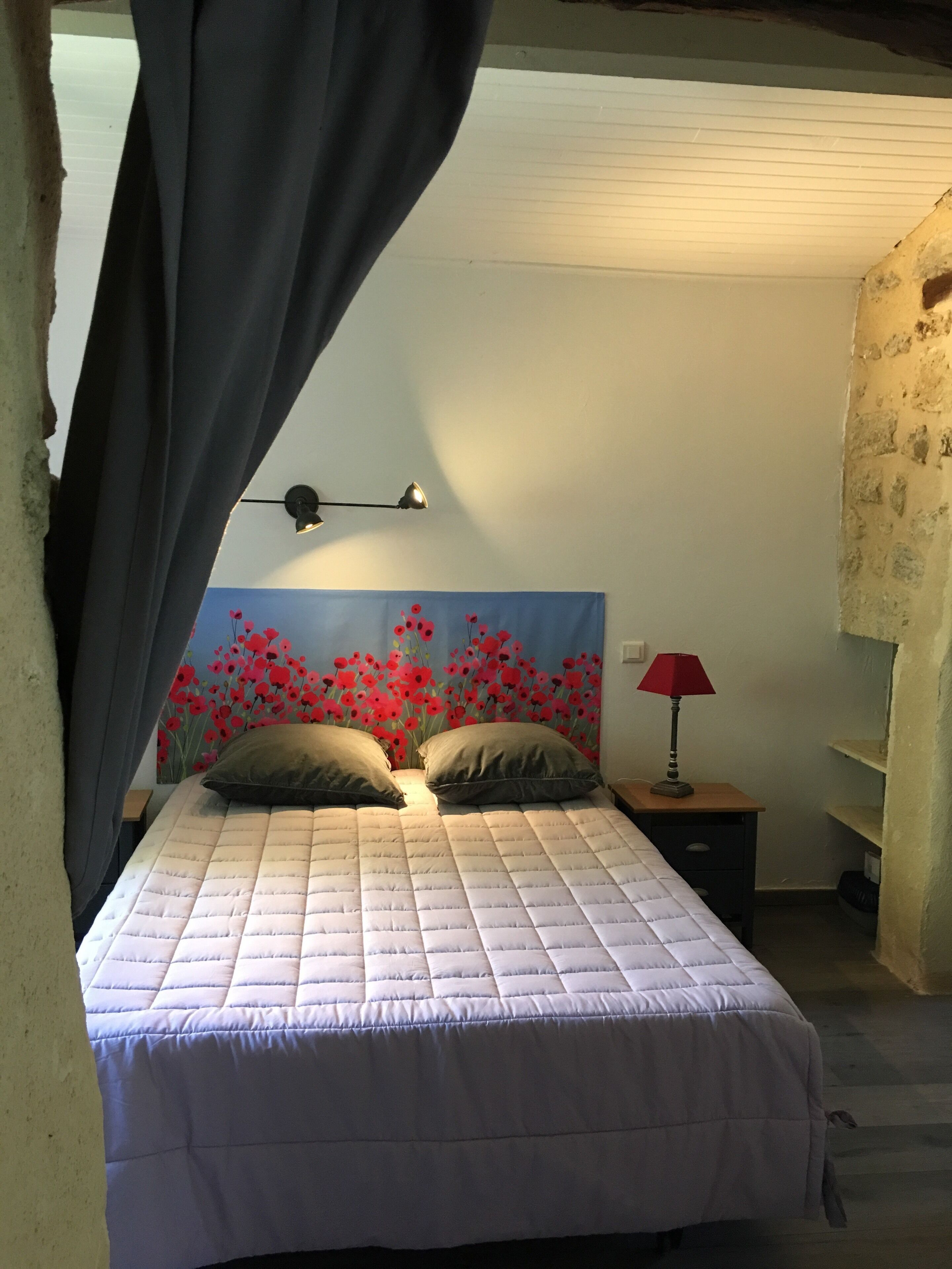 A bed with a quilted cover, two pillows, a bedside lamp, and a wall with a floral mural.
