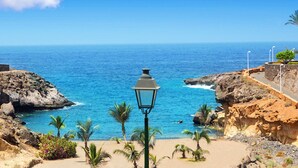A coastal scene with a street lamp, rocky cliffs, and palm trees.