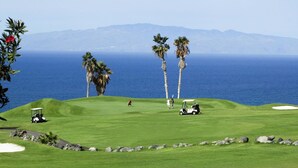 A golf course with a view of the ocean and mountains in the background.