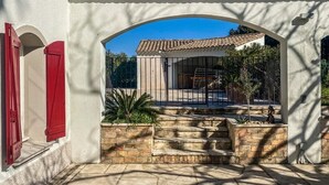A courtyard with a white building, red shutters, and a tiled roof. - Large villa surrounded by pine trees in Provence (Sernhac)