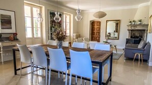 A spacious dining area with a wooden table and white chairs, a fireplace, and a large mirror on the wall. - Large villa surrounded by pine trees in Provence (Sernhac)
