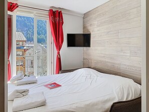 Une chambre d’hôtel avec un lit, un téléviseur fixé au mur et une fenêtre avec des rideaux.