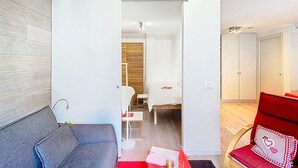 A modern living room with a grey sofa, a red coffee table with a bottle and glasses, a red chair with a heart design, and a wooden floor.