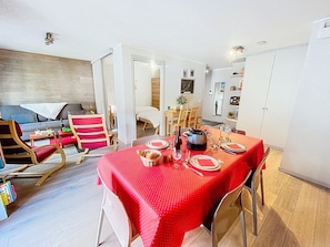 A dining area with a red tablecloth, wooden chairs, and a dining table set with plates, glasses, and a bottle.
