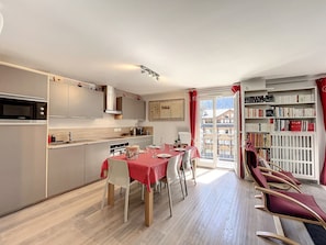 A modern kitchen with a dining area, a bookshelf, and a view of a mountain.