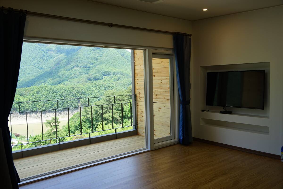 Une pièce dotée d’une grande porte-fenêtre coulissante donnant sur un balcon avec vue sur une colline boisée.