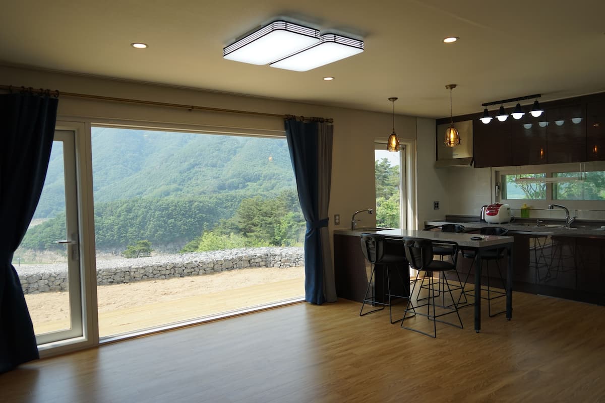 Une cuisine moderne dotée d’un grand îlot central, de tabourets de bar et offrant une vue sur une zone boisée grâce à de grandes portes coulissantes en verre.