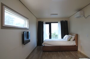 A bedroom with a bed, a TV mounted on the wall, and a window with curtains.
