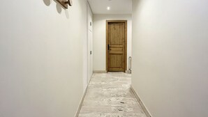 A narrow hallway with a wooden door at the end, white walls, and a light-colored floor. - Cozy Apartment in Chamonix, 4 Pers, Near Brévent with Terrace and Parking (Chamonix-Mont-Blanc)