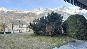A building with a stone facade, a lawn, and a mountain backdrop. - Cozy Apartment in Chamonix, 4 Pers, Near Brévent with Terrace and Parking (Chamonix-Mont-Blanc)