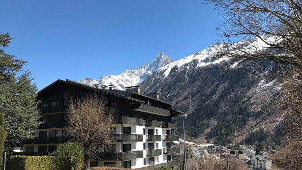 A multi-story hotel with balconies, set against a backdrop of snow-capped mountains and a clear blue sky. - Cozy Apartment in Chamonix, 4 Pers, Near Brévent with Terrace and Parking (Chamonix-Mont-Blanc)