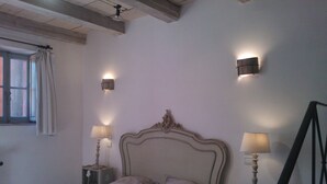 A bedroom with a bed, two bedside lamps, a window with curtains, and a wall-mounted light fixture.
