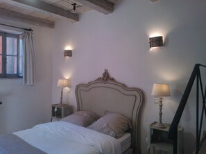Um quarto com uma cama, duas luminárias de cabeceira, uma janela com cortinas e um ponto de luz fixado na parede.