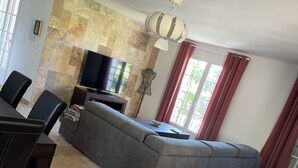 Una sala de estar con un sofá seccional gris, un televisor de pantalla plana y un comedor con mesa y sillas.