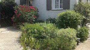 Una casa con techo de tejas, una ventana con contraventanas y un jardín con diversas plantas y flores.