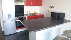 Una cocina compacta con refrigerador, estufa, microondas y gabinetes rojos.